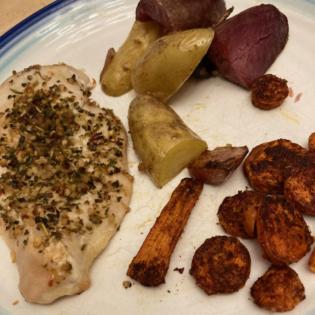 Roasted chicken, potatoes, and carrots on a white plate with blue trim.