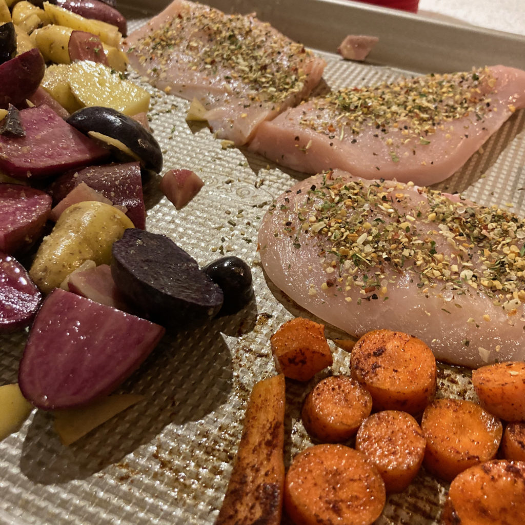 Chicken, potatoes, and carrots on a beige sheet pan ready to go in the oven.