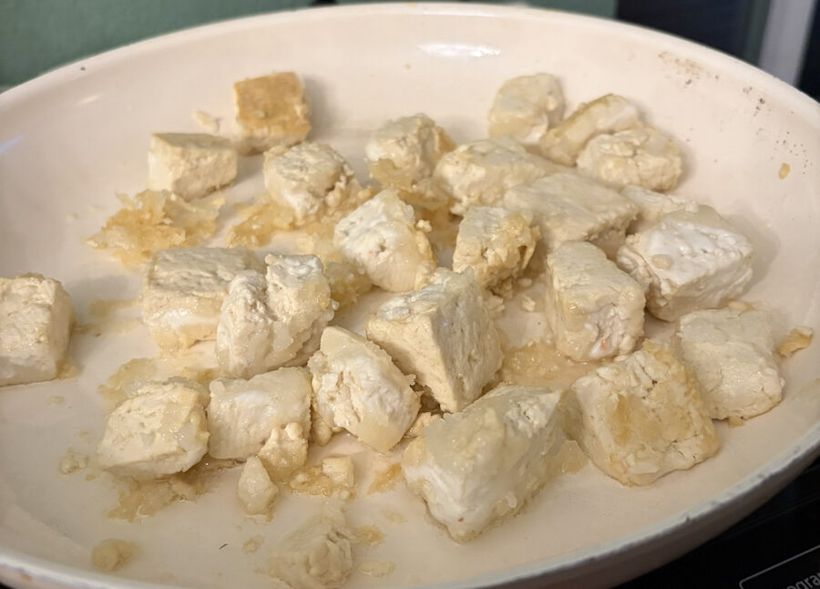 Tofu coated in cornstarch cooking in a pan.