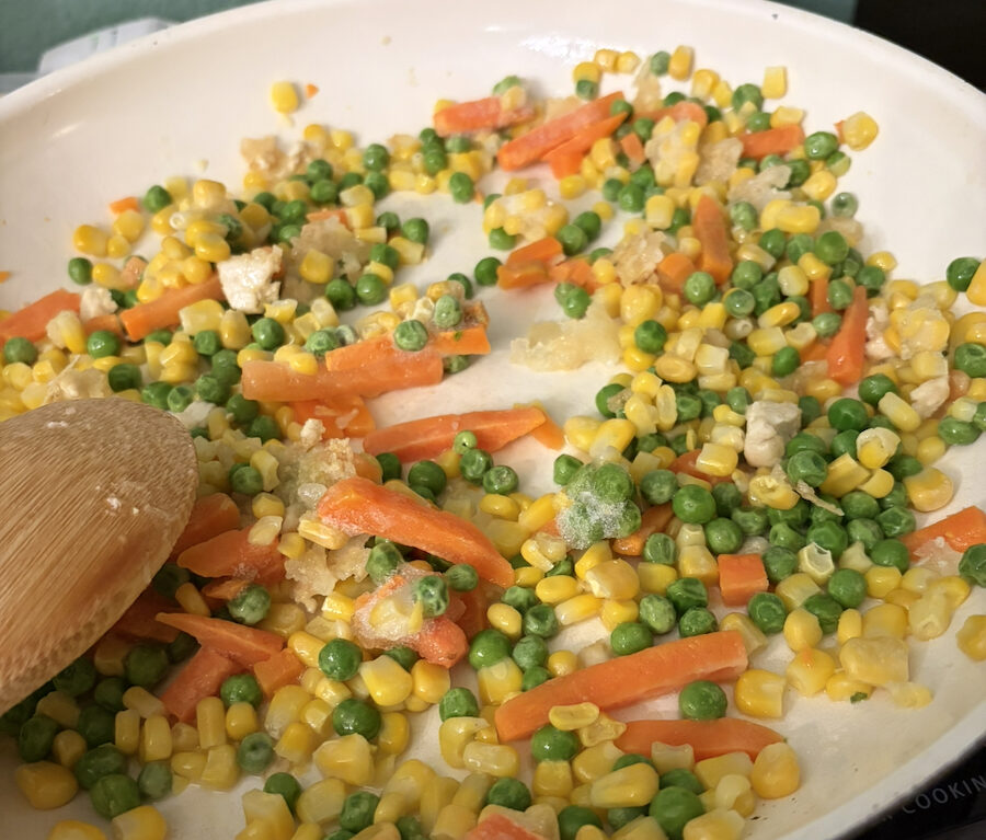 Frozen corn, peas, and carrots cooking in a pan.